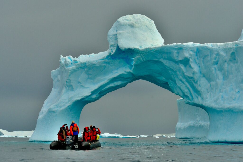 boaters sailing under a hole in an iceberg