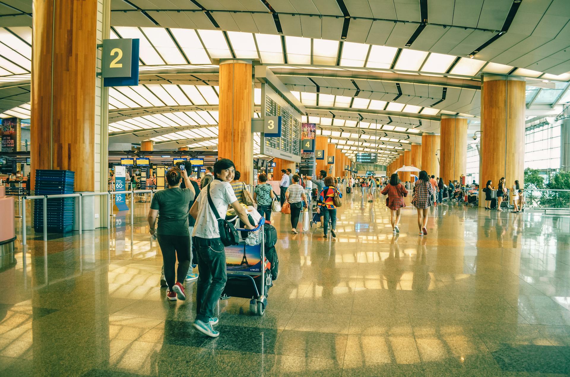 person smiling at the camera pushing a full luggage cart through a busy airport