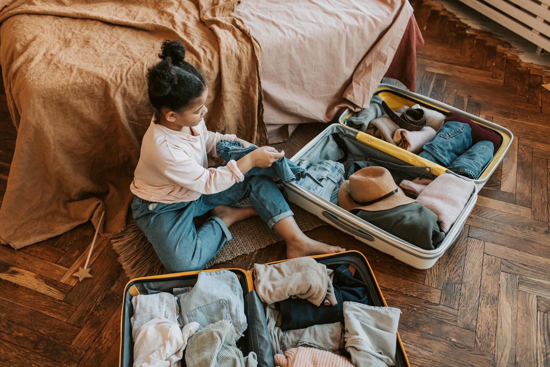 young girl sitting on the floor with two open suitcases in front of her.