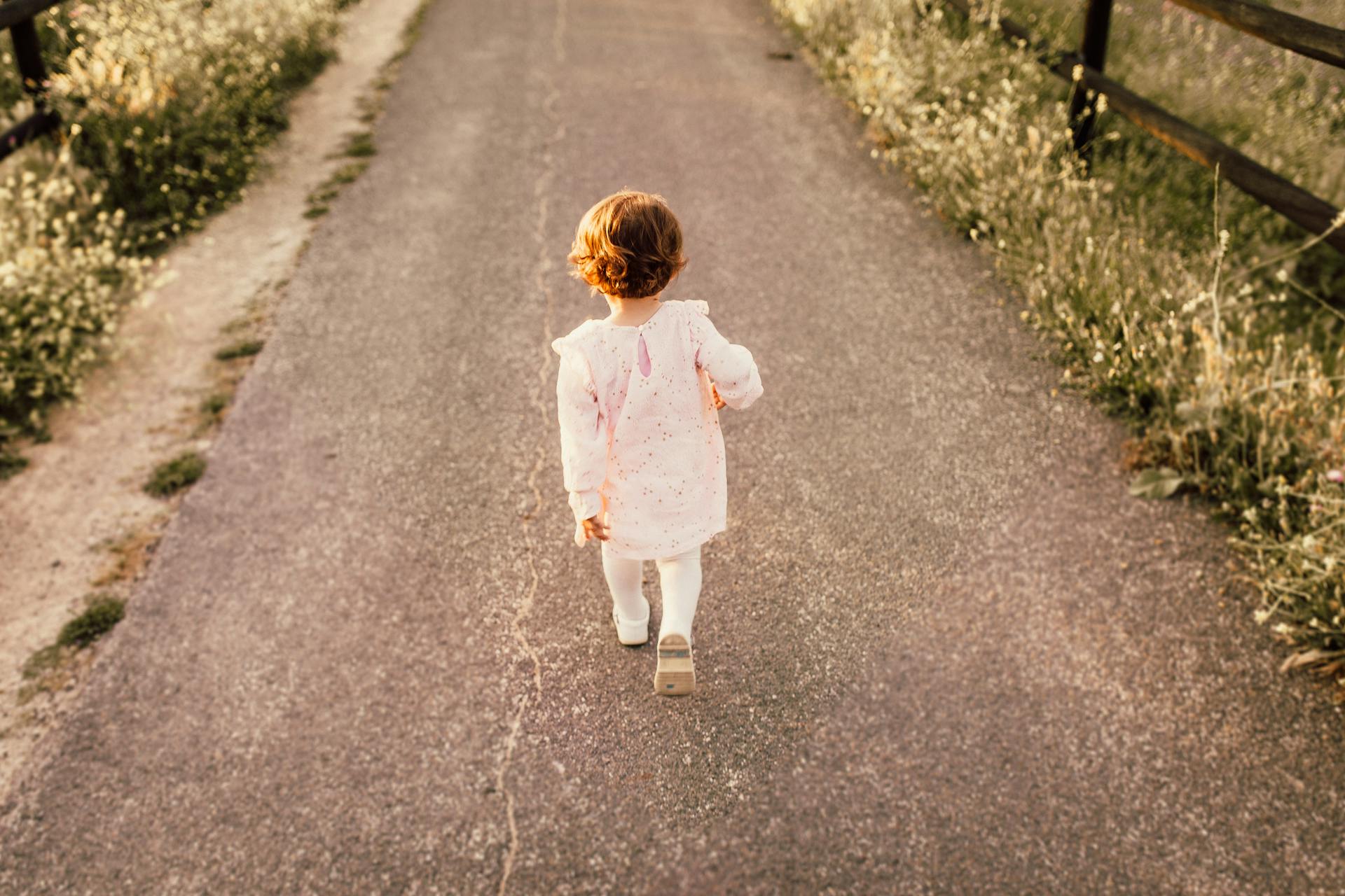 small child wearing white walking on paved sidewalk