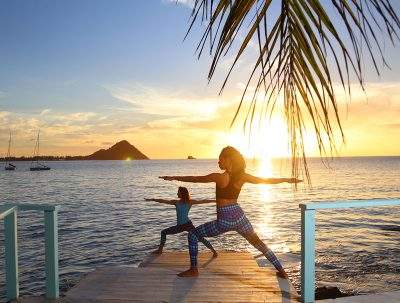 two women doing yoga near the water at sunset 