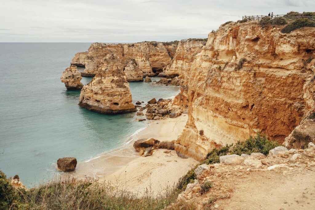 Brown rock formations jutting out to sea nearby a small beach in Portugal