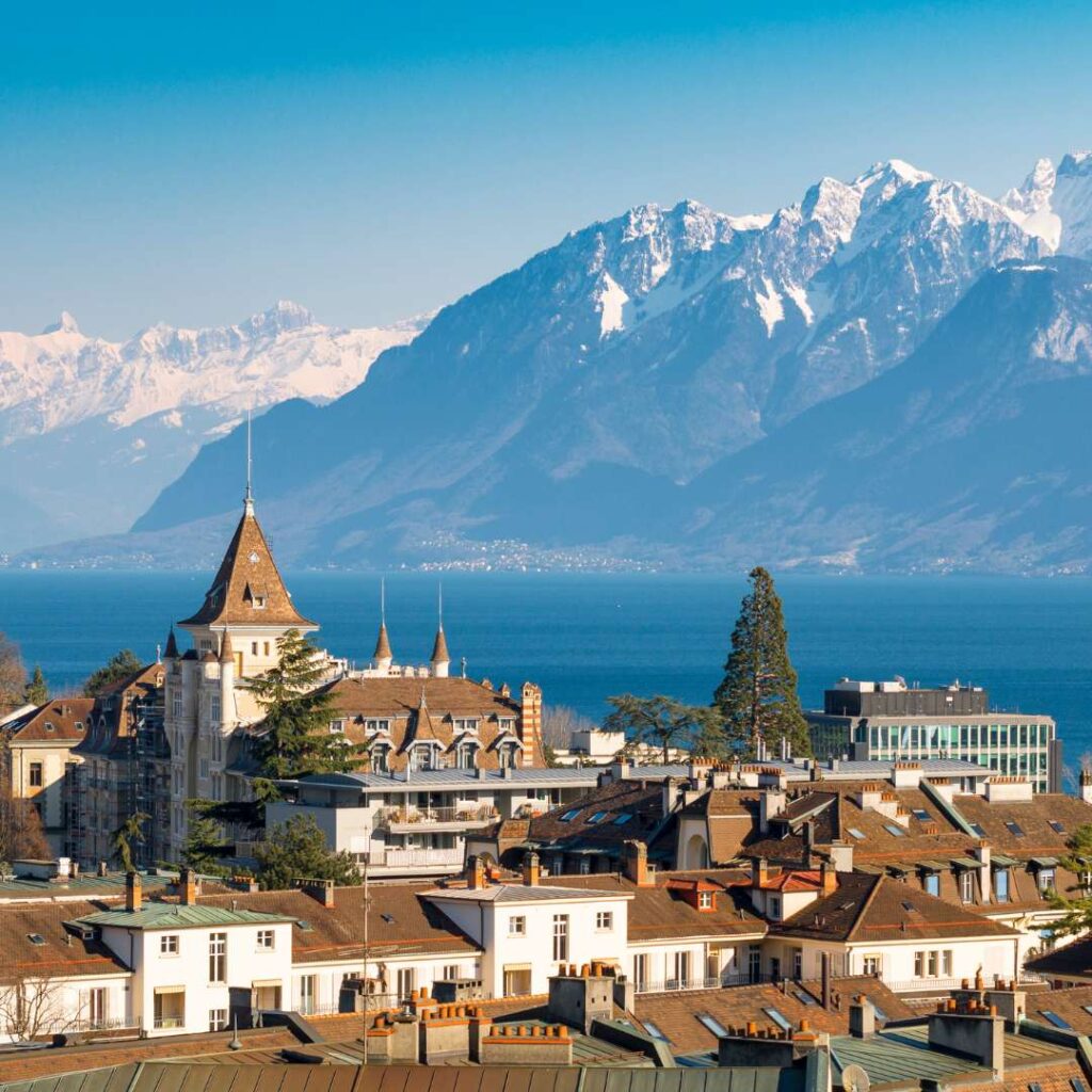 some buildings in lausanne switzerland with a large body of water and mountains behind them