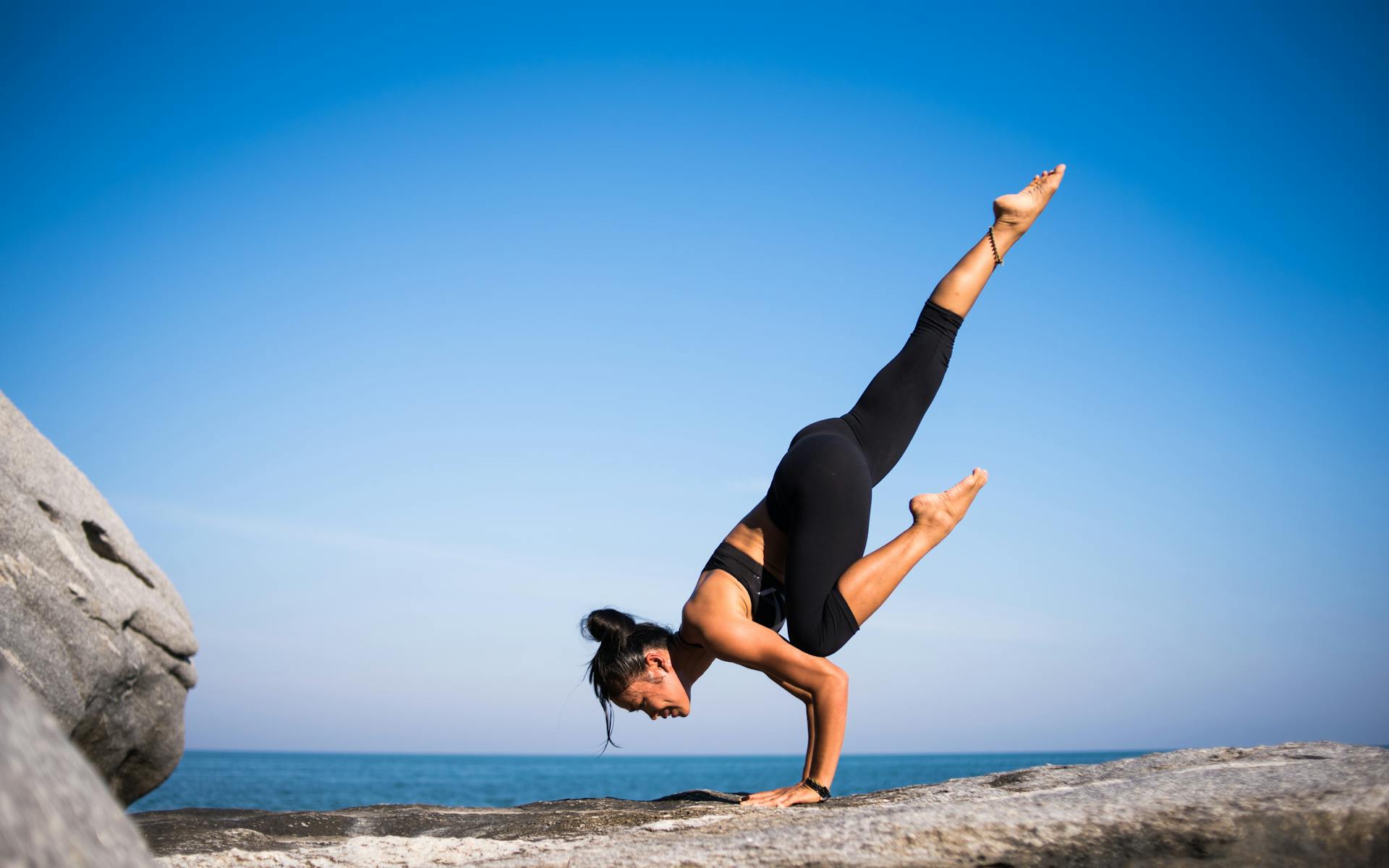 Low Angle View of Woman in intense yoga pose on Beach Against Blue Sky