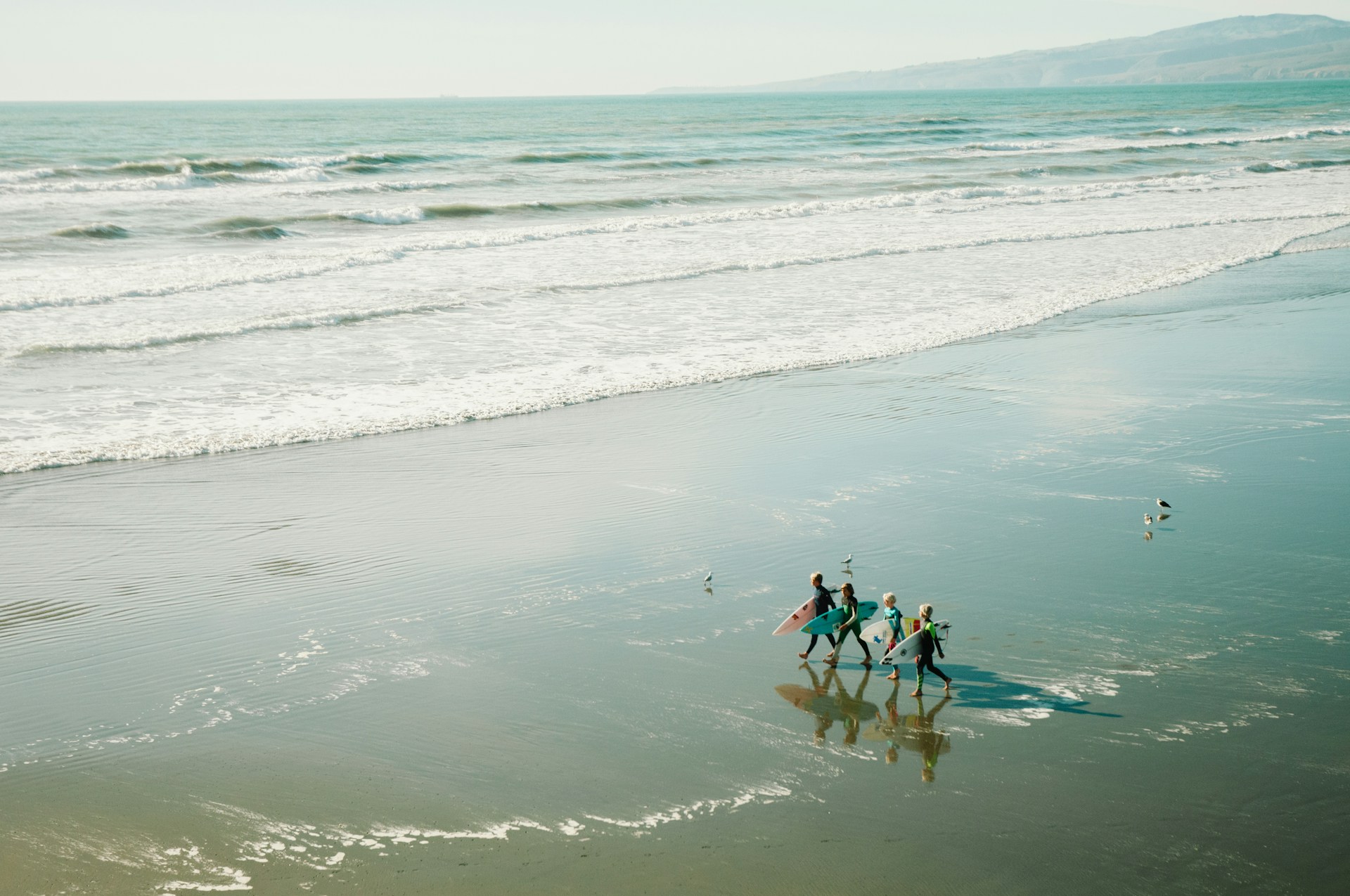 a family carrying surfboards walking along seashore in new zealand