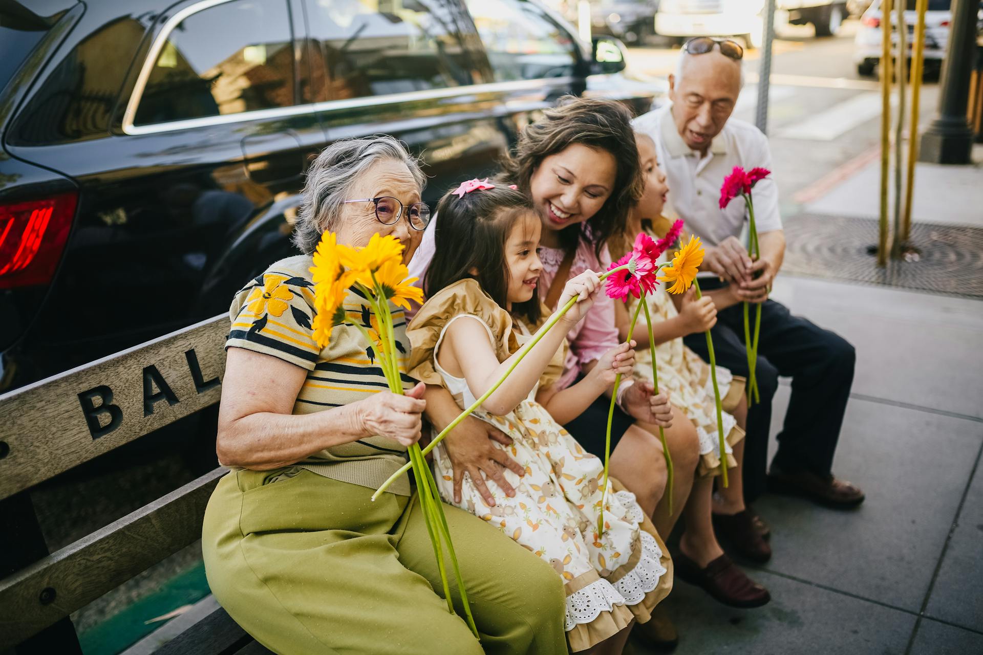 a happy family multigenerational family sitting on a bench holding flowers laughing