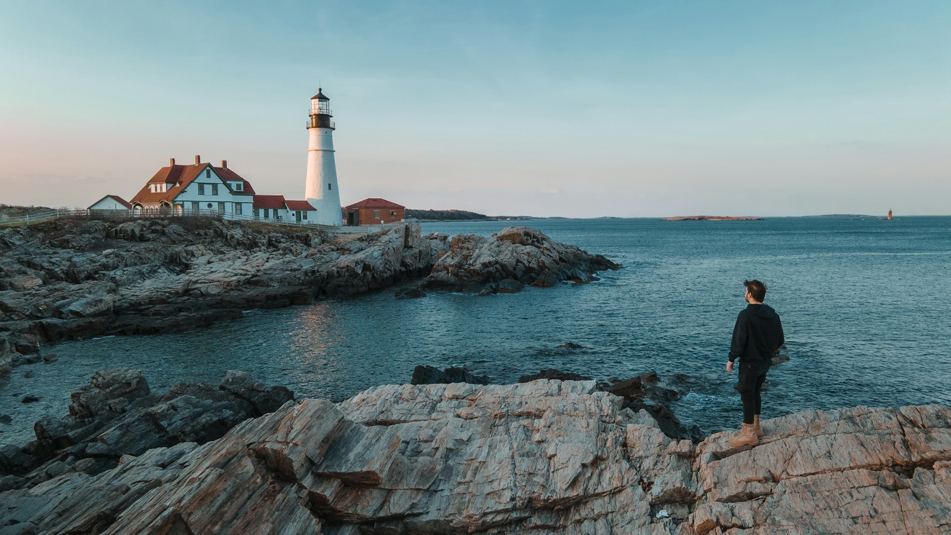 a man standing on a rock looking at a lighthouse somewhere in maine