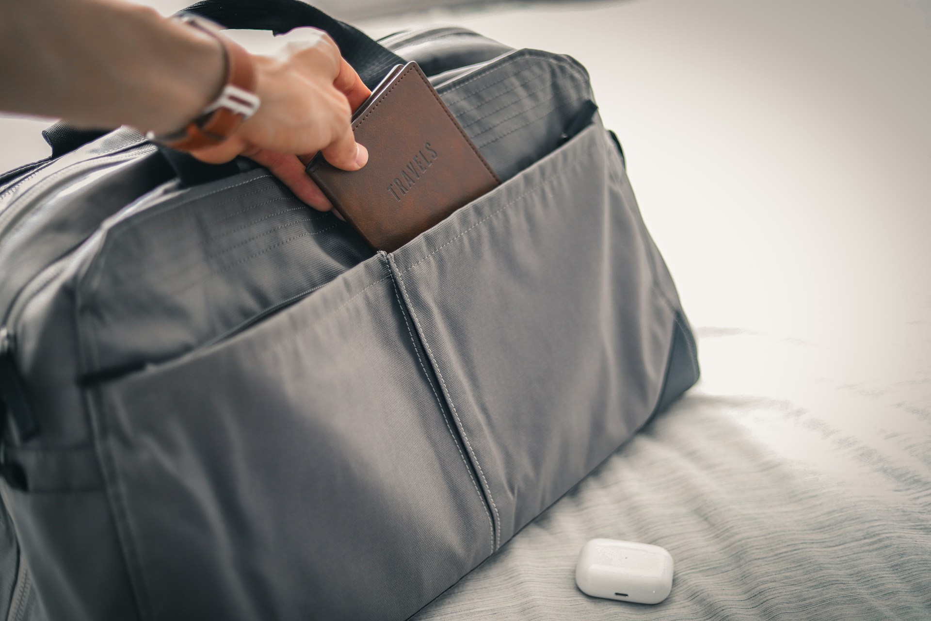 a person putting a wallet into a closed and full duffel bag on a bed