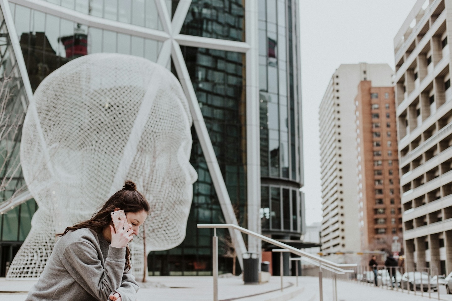 a woman sitting near a statue in a city talking on a phone