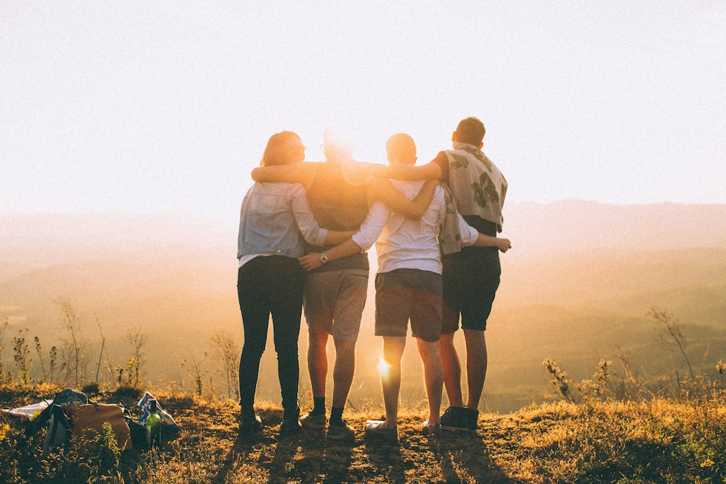 four person hands wrapped around shoulders while looking at the sunset