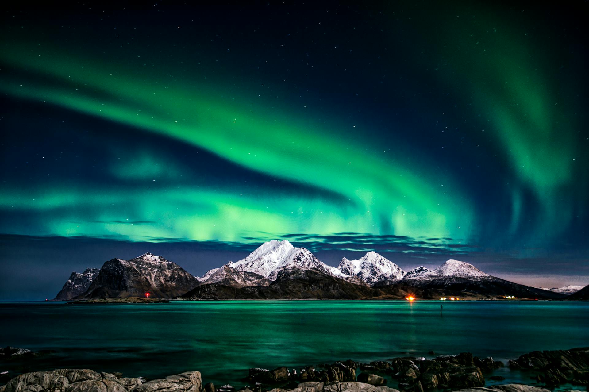 green northern lights against a black sky and snow capped mountains