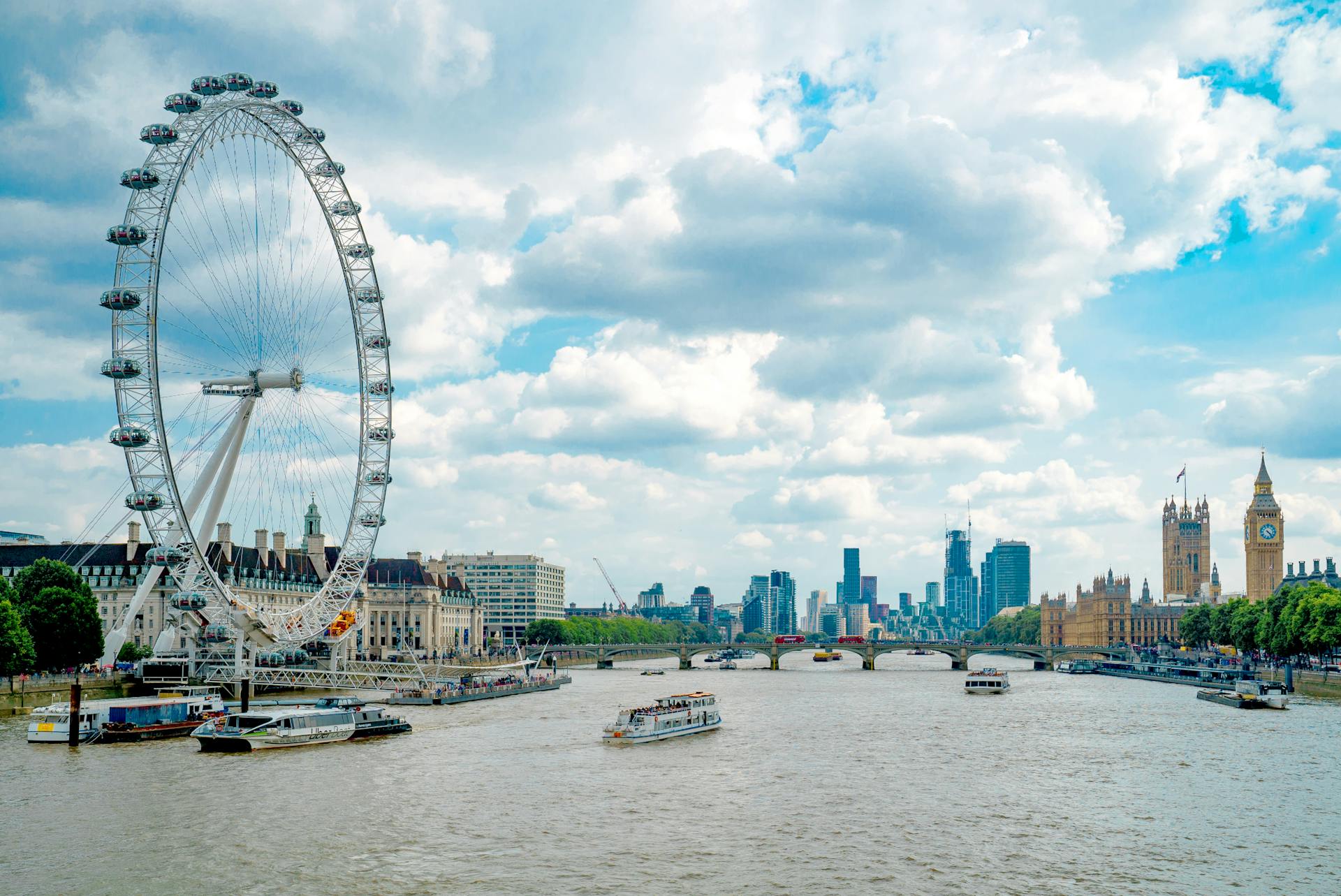 white boat on the thames river in London near city buildings and the eye ferris wheel