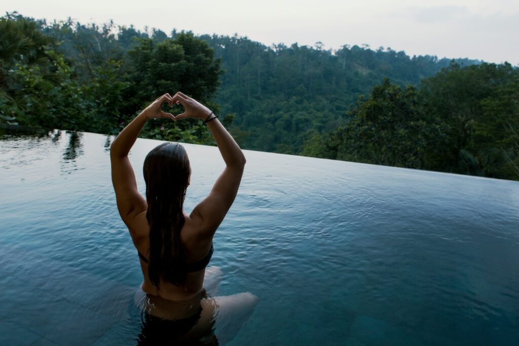 woman in relaxing infinity pool facing forest