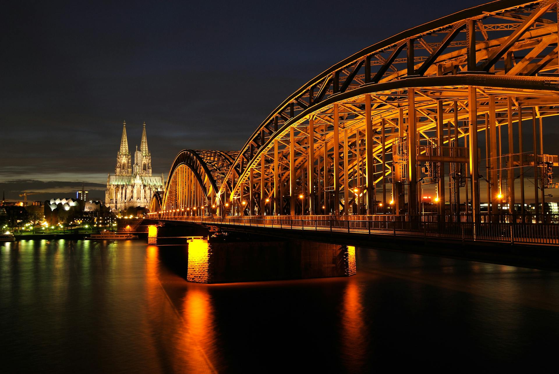 Illuminated Cologne Cathedral and Hohenzollern Bridge at night as seen from the Rhine