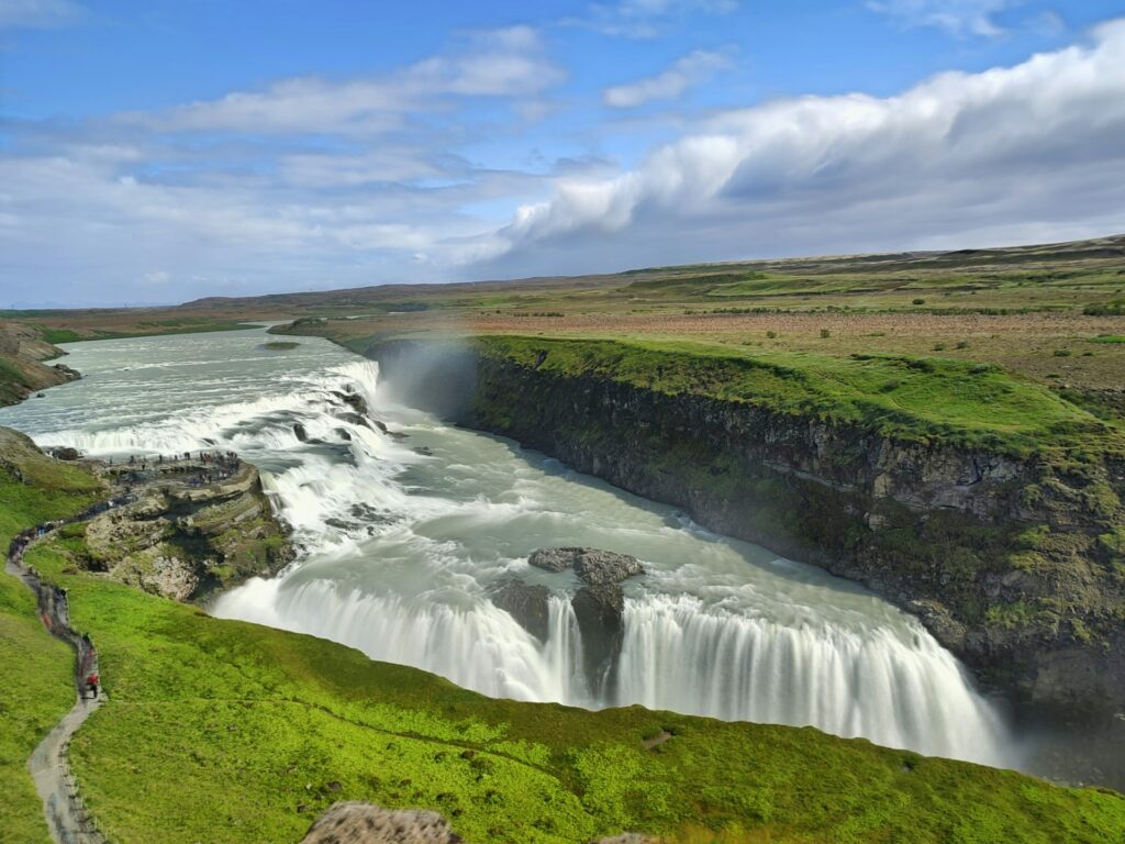 Golden circle walking trail in iceland. Green land as far as the eye can see cut down the middle by a wide flowing river with cascading rock drops