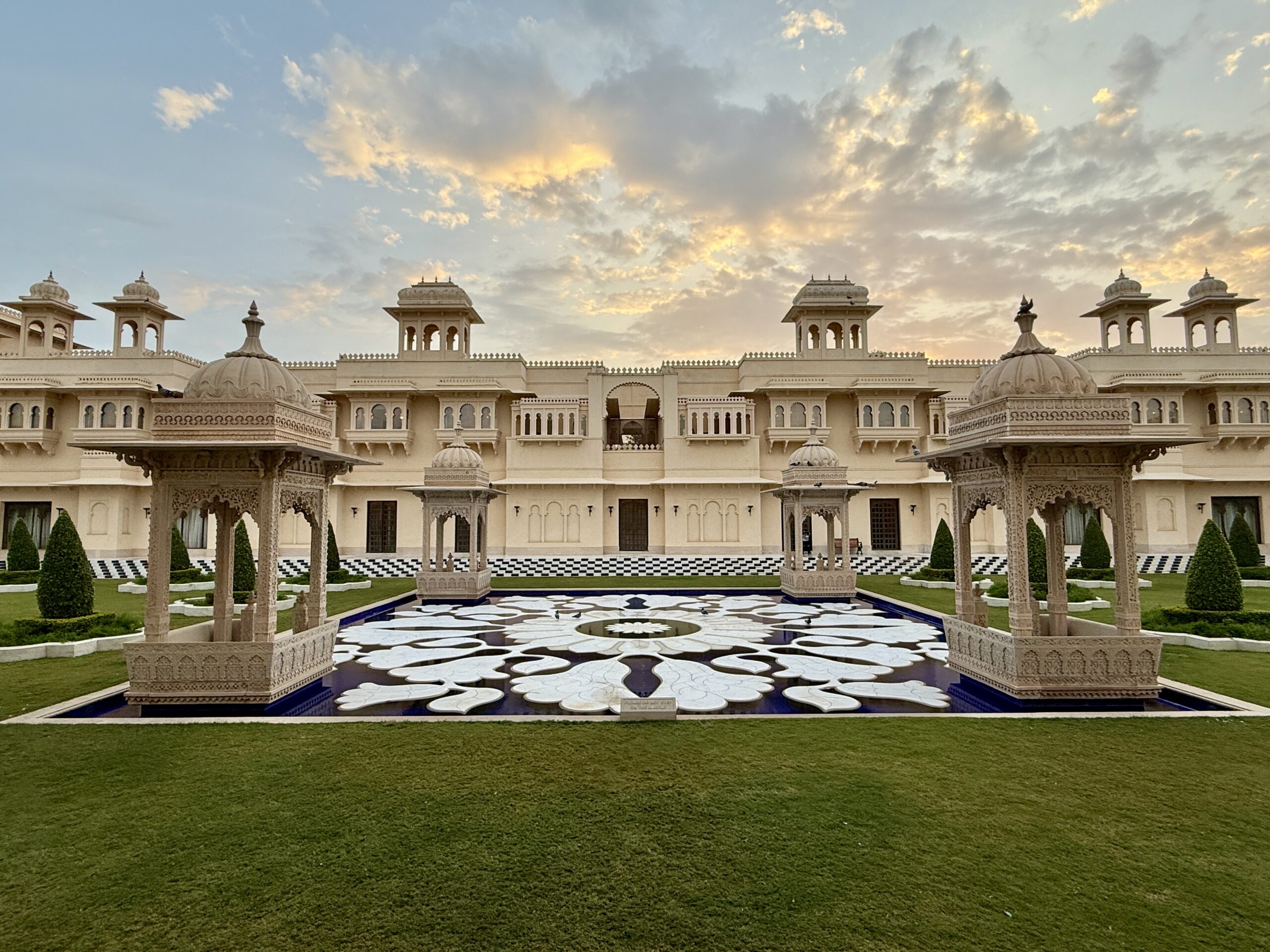 The Oberoi Udaivilas in Udaipur at sunset, with a white marble lotus pool framed by carved sandstone pavilions in front of the domed palace facade