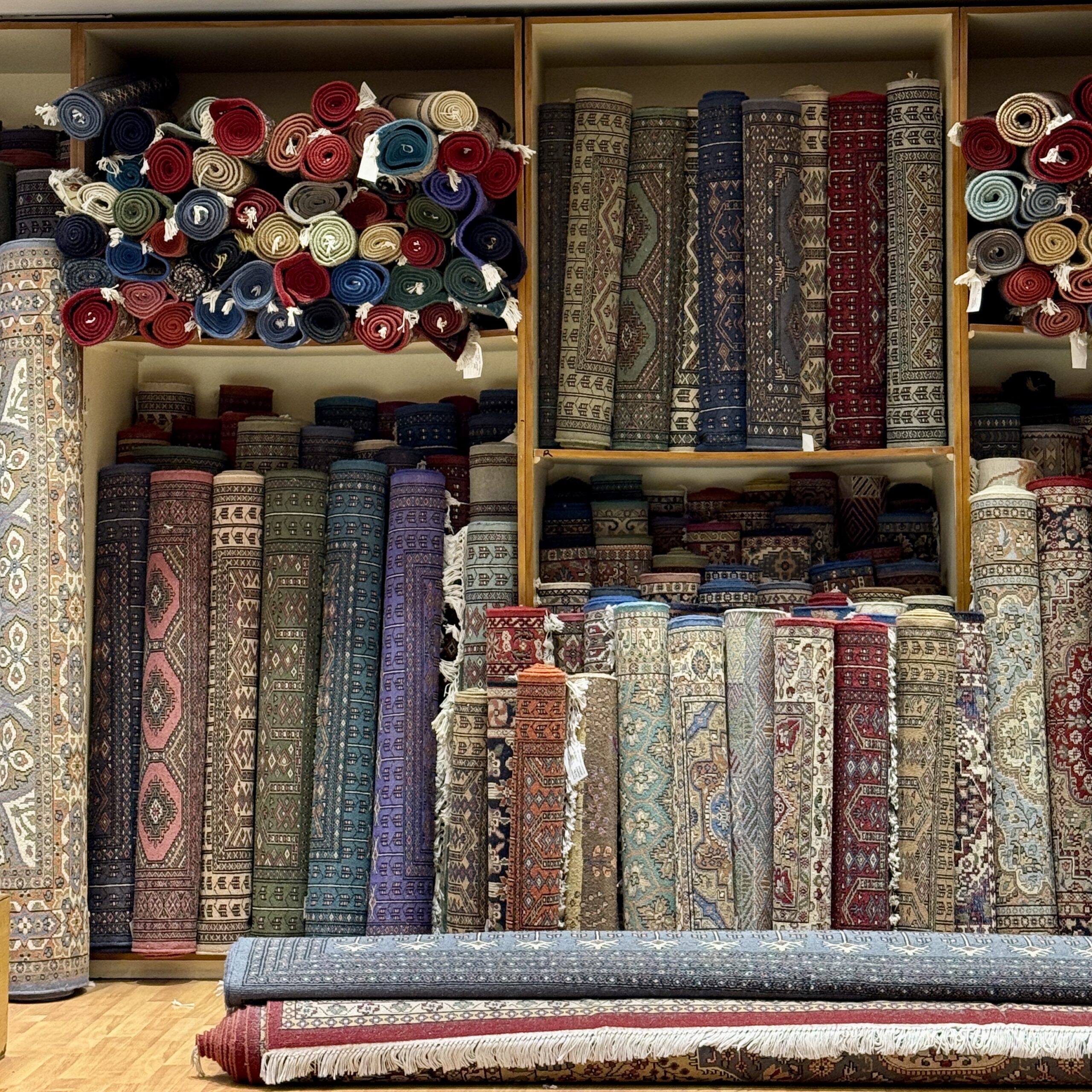 Shelves of rolled hand-knotted carpets in reds, blues, greens and purples, stacked floor to ceiling in an Indian carpet showroom