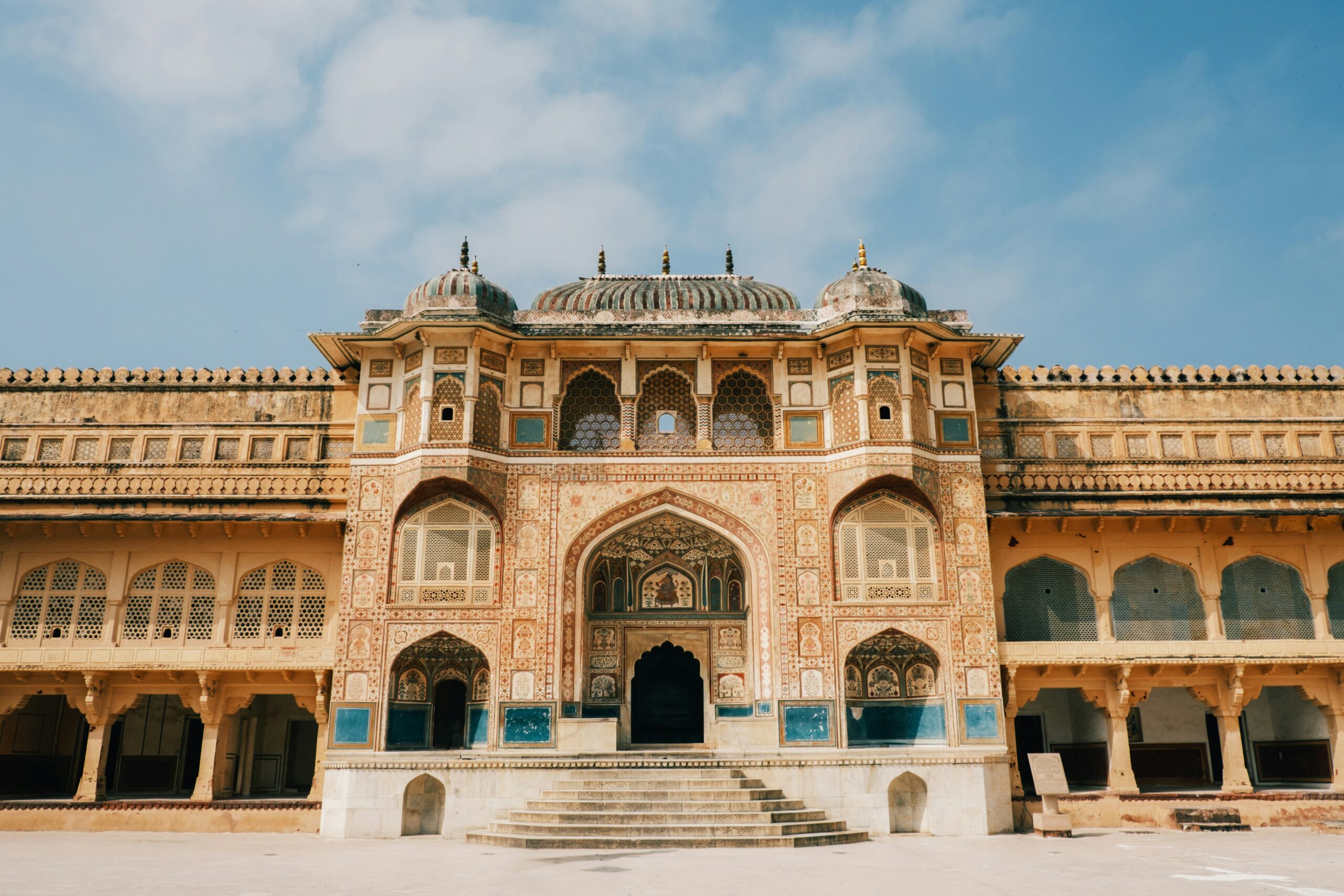 The painted Ganesh Pol gateway at Amber Fort in Jaipur, its frescoed arches and latticed windows facing an empty courtyard under a blue sky